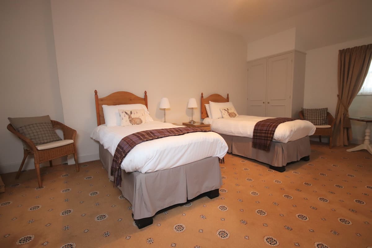 Habitación de hotel con dos camas, una silla, un armario y una ventana con cortinas.