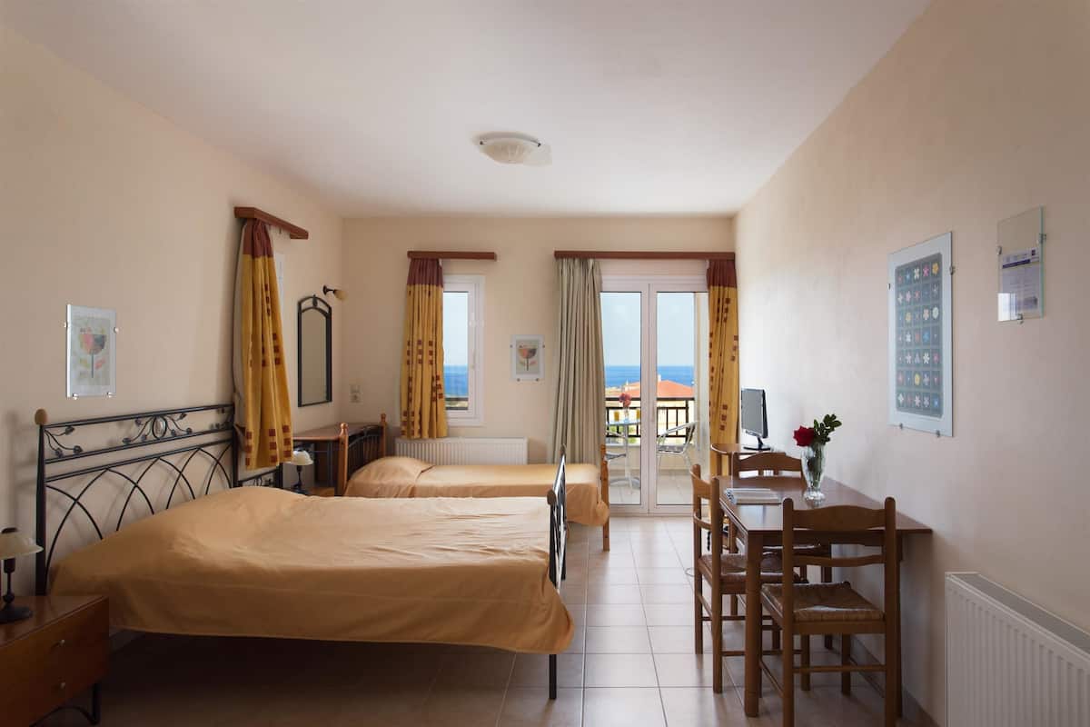 Ein Hotelzimmer mit zwei Betten, einem Schreibtisch mit Stuhl, einem Fenster mit Vorhängen und Blick aufs Meer.
