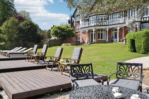 A courtyard with sun loungers and a table with cups, surrounded by a large house with a balcony. - River Arts Club (Maidenhead)