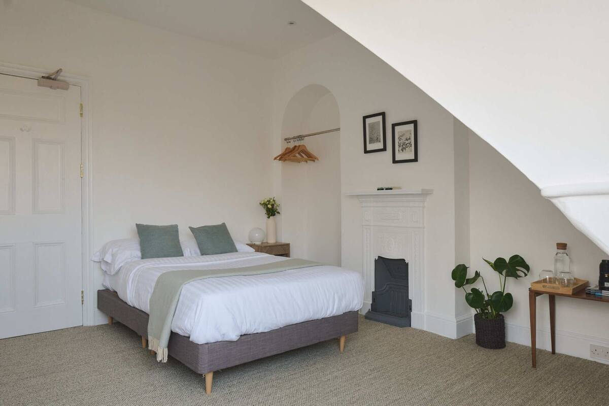 A bedroom with a bed, a nightstand, a dresser, a hanging coat rack, and a potted plant.