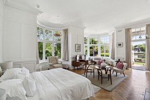 A spacious bedroom with a large bed, a desk, and a seating area by the window. - River Arts Club (Maidenhead)