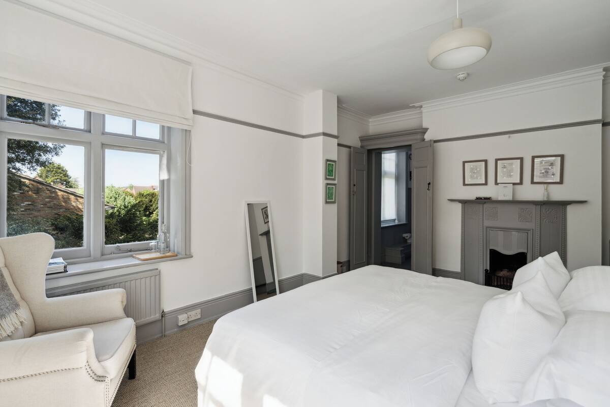 A bedroom with a large bed, a chair, a window, and a fireplace.