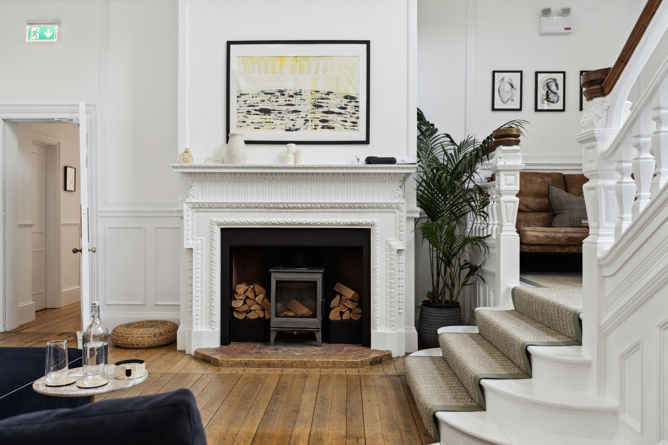 A living room with a fireplace, a staircase, and a large framed artwork on the wall.