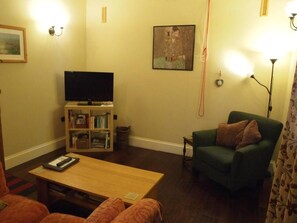 A living room with a flat-screen TV, a bookshelf, a green armchair, and a table. - The Stables at Owlett Hall (Scunthorpe)