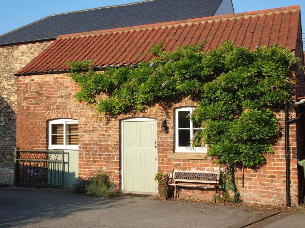 A brick building with a green door, a bench, and a garden area.