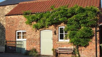 A brick building with a green door, a bench, and a garden area.