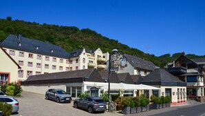 A hotel with a traditional European architectural style, featuring multiple windows and balconies. There are parked cars in front, and the hotel is situated on a hillside with a clear view of the surrounding landscape. - Schloß-Hotel Petry (Treis-Karden)