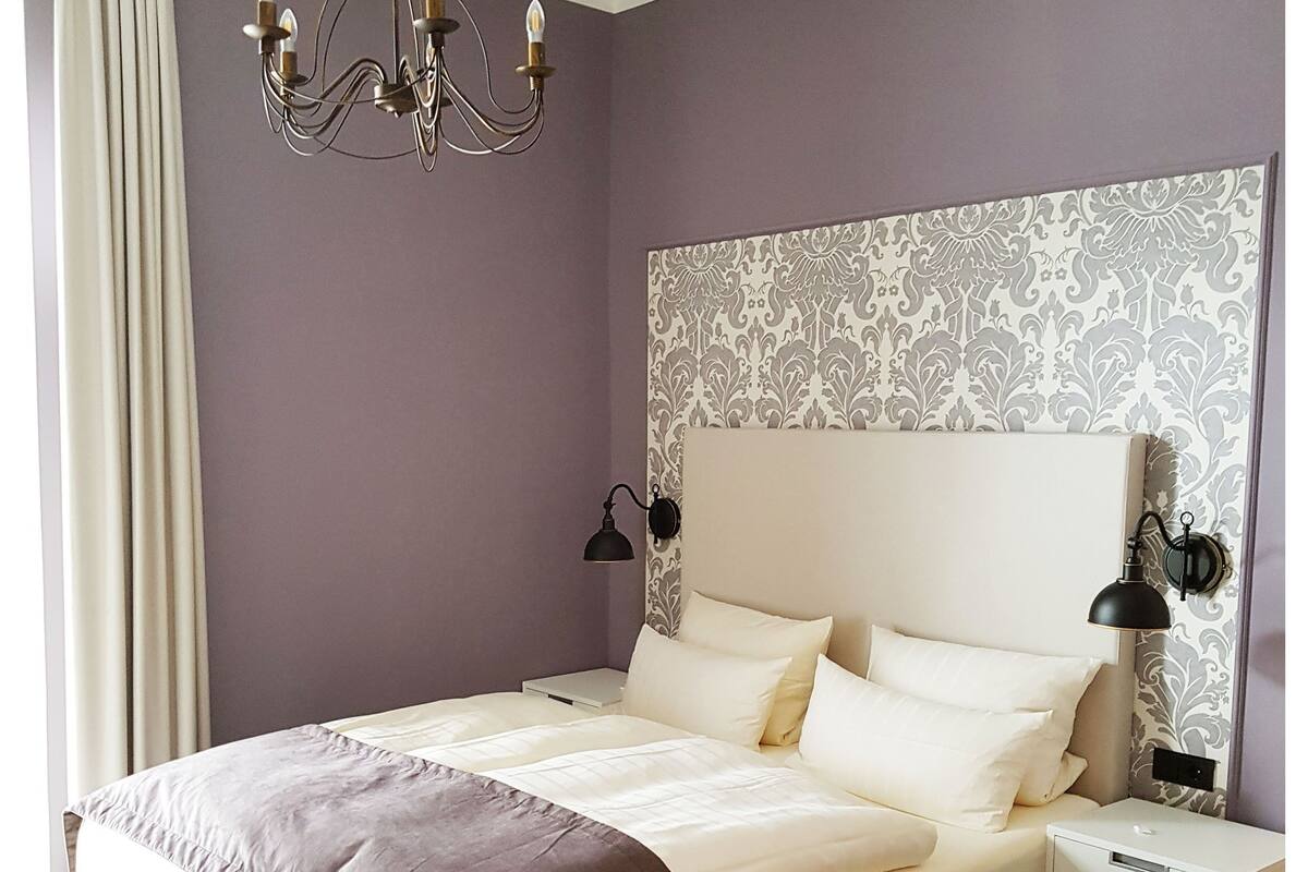 Een slaapkamer met een groot bed, bedlampen, een kroonluchter, een nachtkastje en een klein tafeltje.