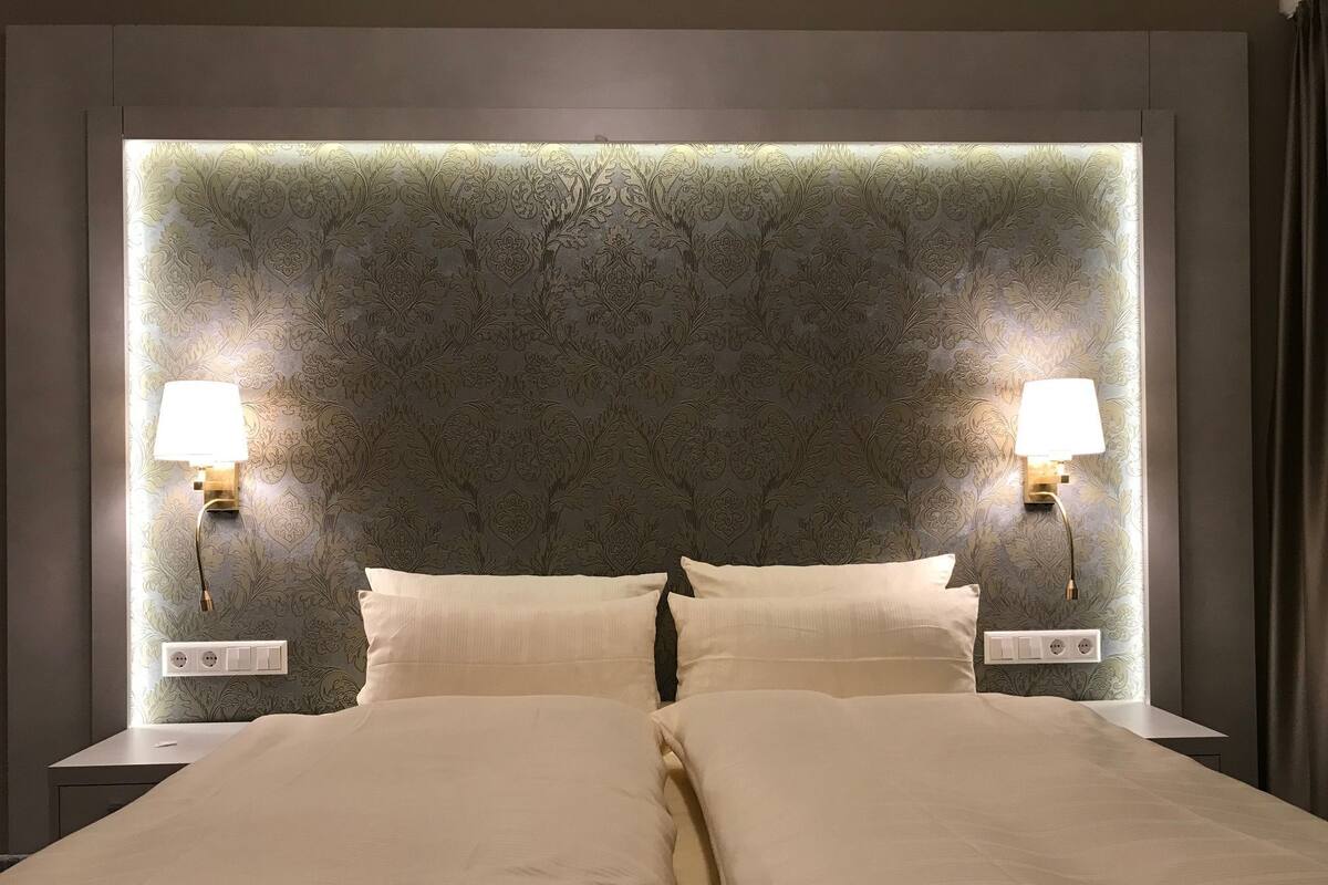 Een hotelkamer met een groot bed, twee bedlampjes en een gestructureerde muur achter het bed.
