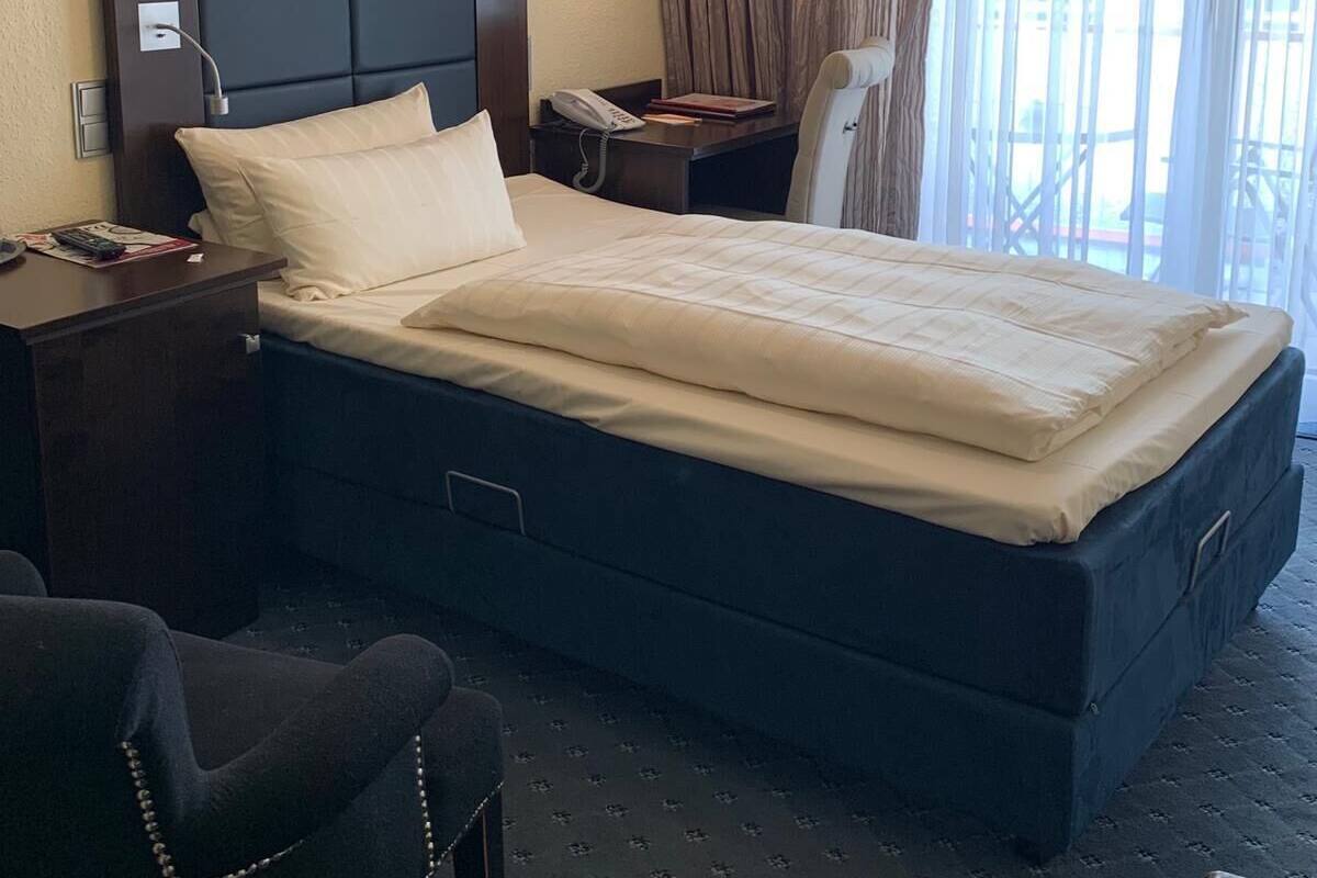 Een hotelkamer met een groot bed, een bureau met telefoon, een stoel en een raam met gordijnen.