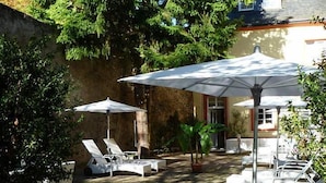 A patio area with sun loungers and umbrellas, surrounded by greenery and a stone wall. - Schloß-Hotel Petry (Treis-Karden)