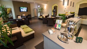 A modern hotel lobby with a seating area, a television, and a kitchen counter with a coffee machine. - Schloß-Hotel Petry (Treis-Karden)