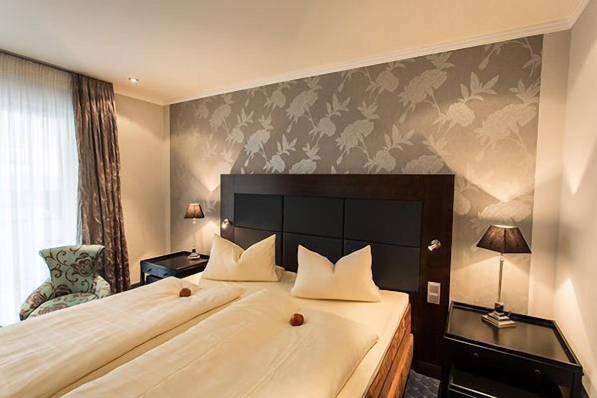Een hotelkamer met een groot bed, twee nachtkastjes, een stoel en een muur met een bloemenpatroon.
