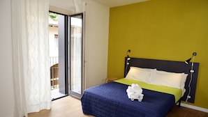 Une chambre avec un lit, un mur vert et une porte-fenêtre coulissante donnant sur un balcon.