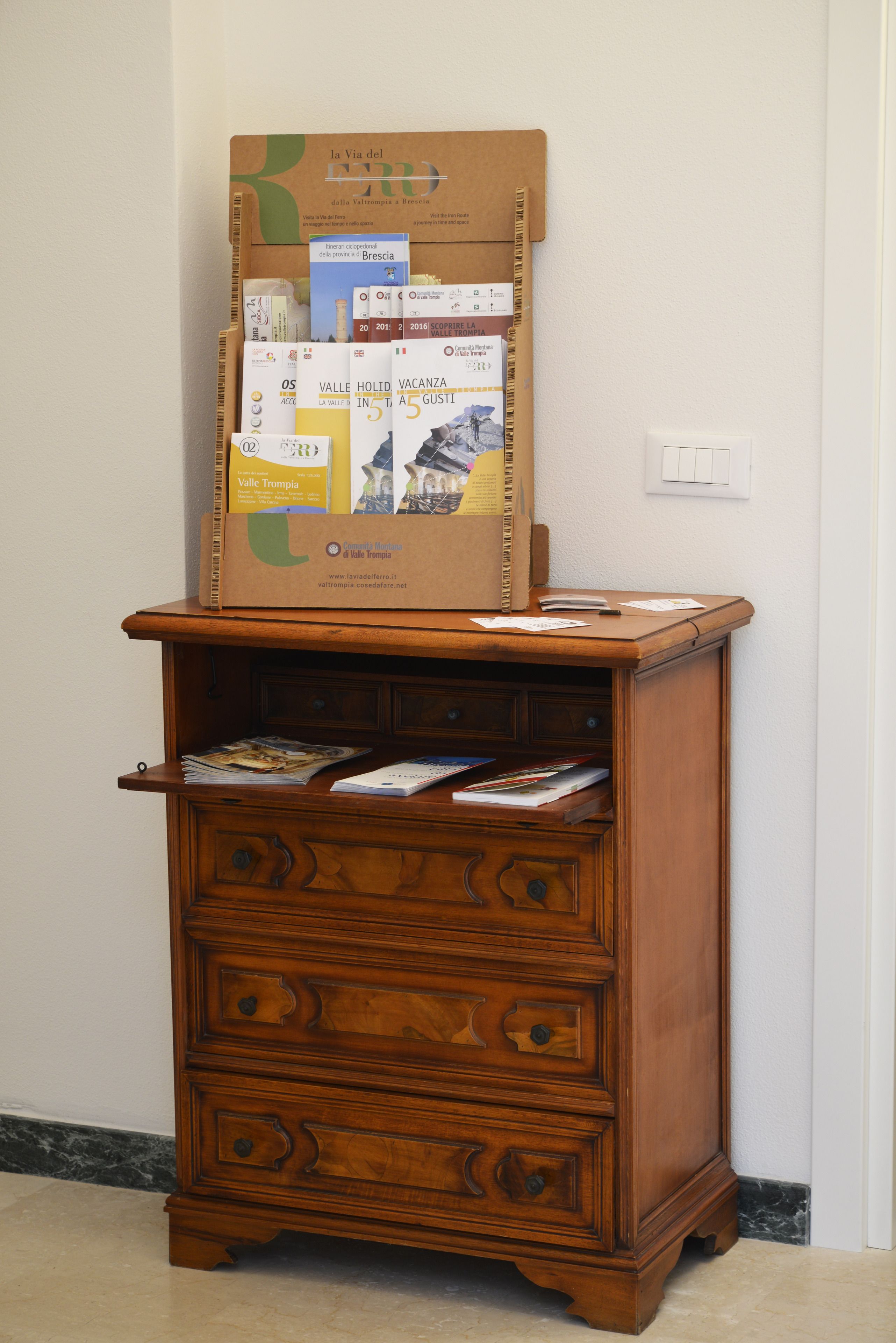 Un aparador de madera con una caja de cartón encima, que contiene varios folletos y mapas.