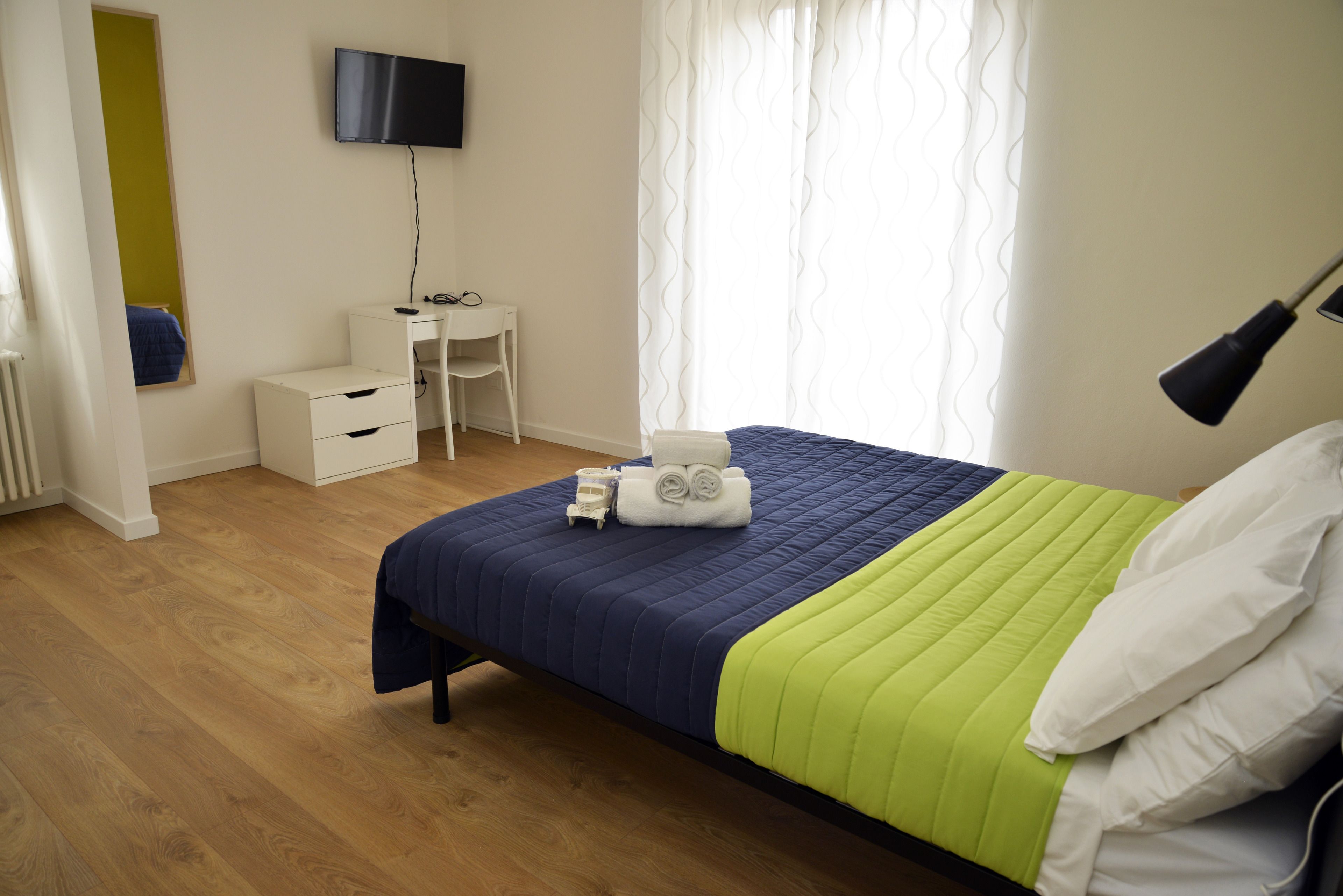 Un dormitorio con cama, escritorio, silla, televisión y ventana con cortinas.