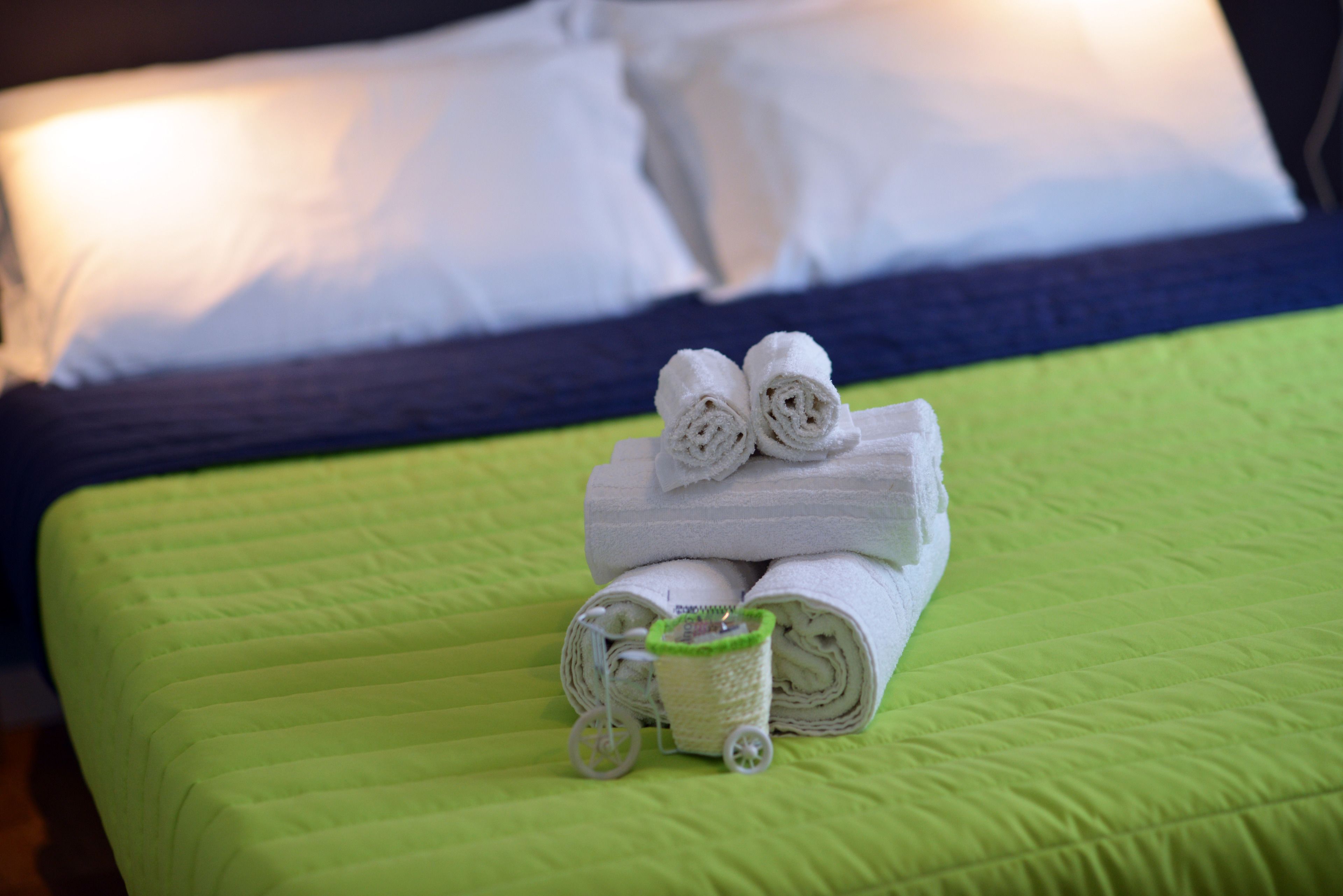 A neatly made bed with green bedding and a rolled towel on top.