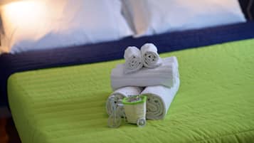 Una cama bien hecha con ropa de cama verde y una toalla enrollada encima.