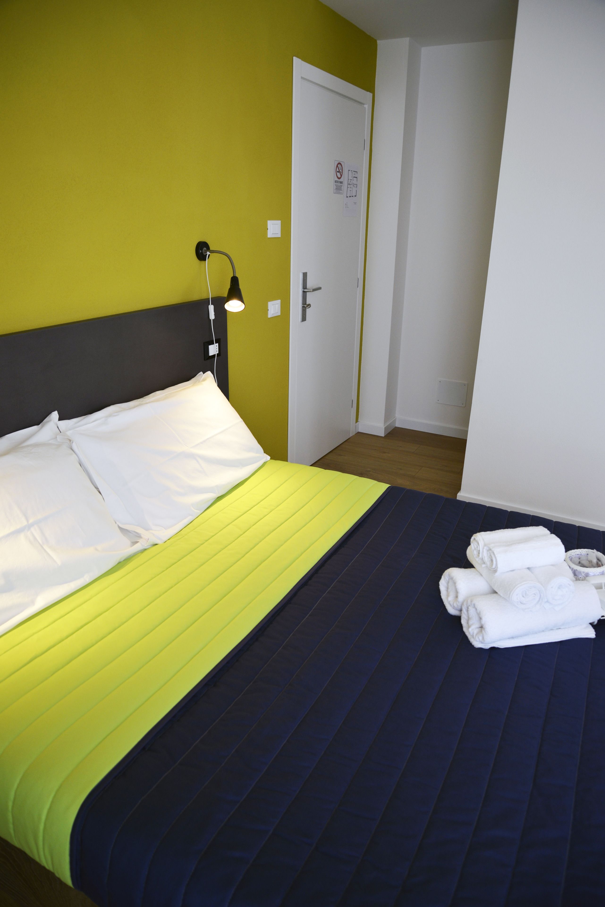 Ein Hotelzimmer mit einem Bett, einem Nachttisch mit Lampe und einer Tür.
