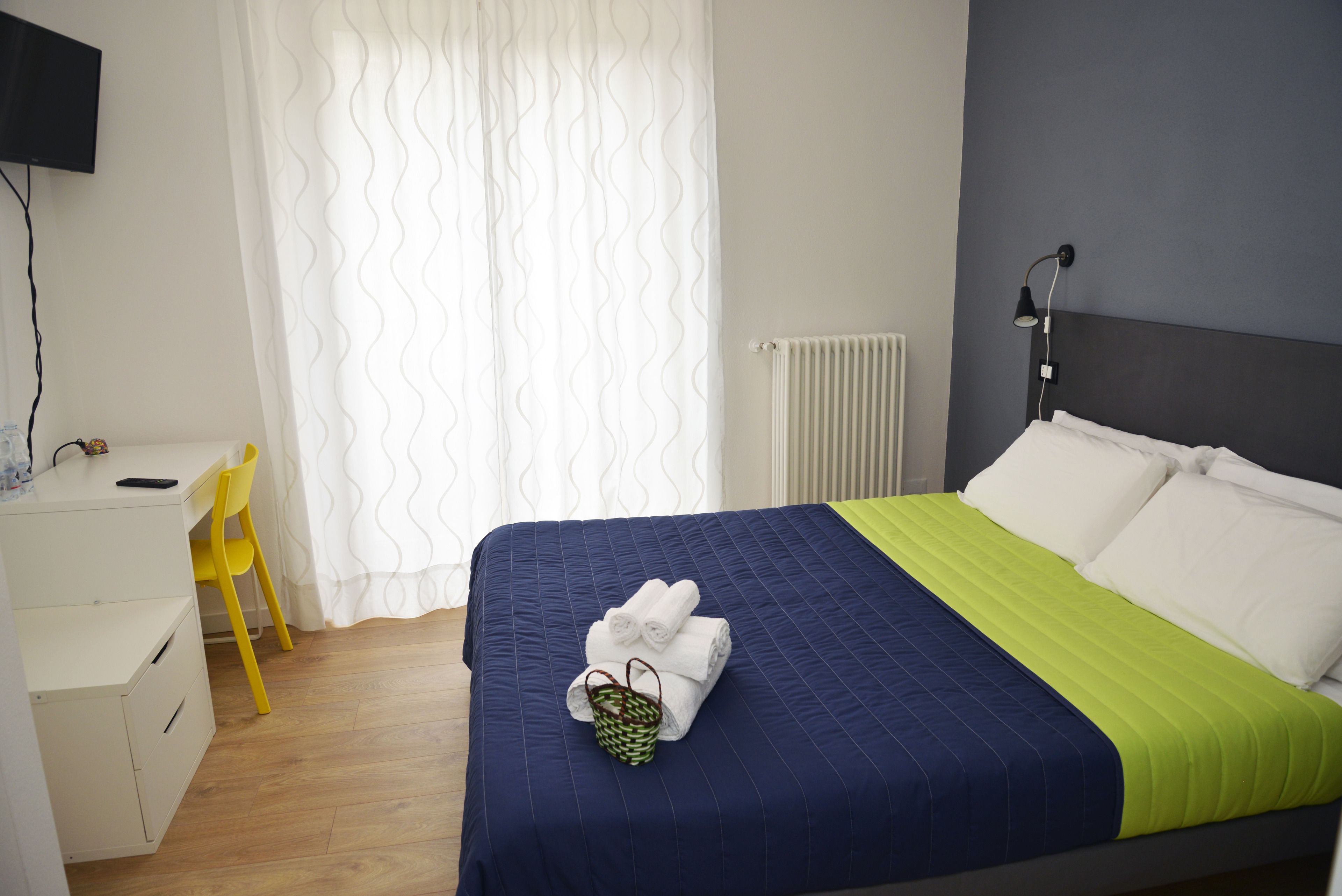 A neatly made bed with a blue and green bedspread, a white pillow, and a green basket with towels.