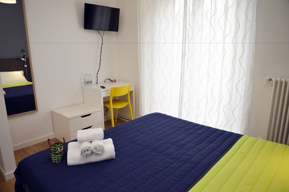 A hotel room with a bed, a desk, a chair, a television, and a window with curtains.