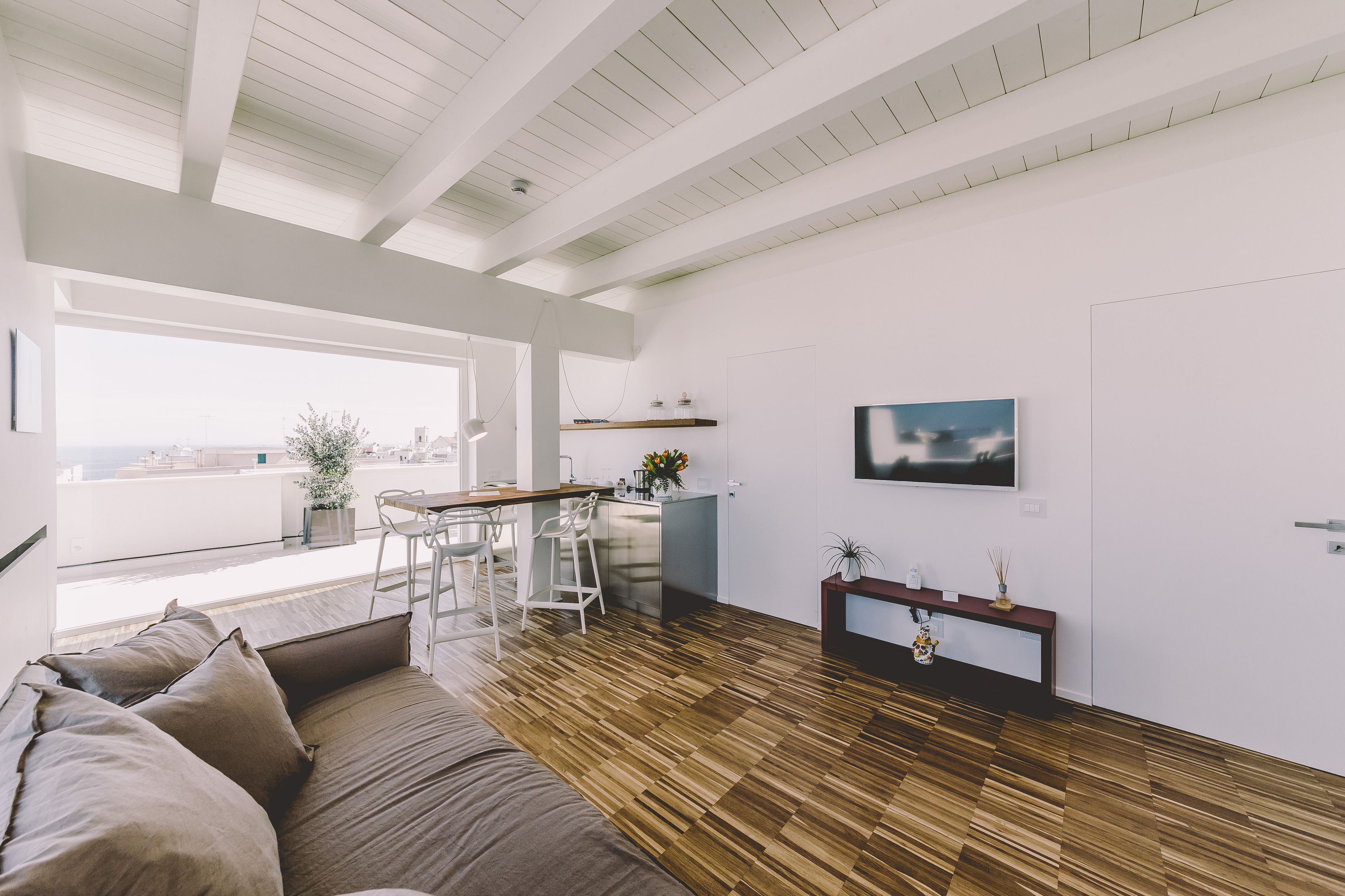 Una sala de estar moderna con piso de madera, un sofá, un comedor con barra y un ventanal que ofrece vistas a la ciudad.