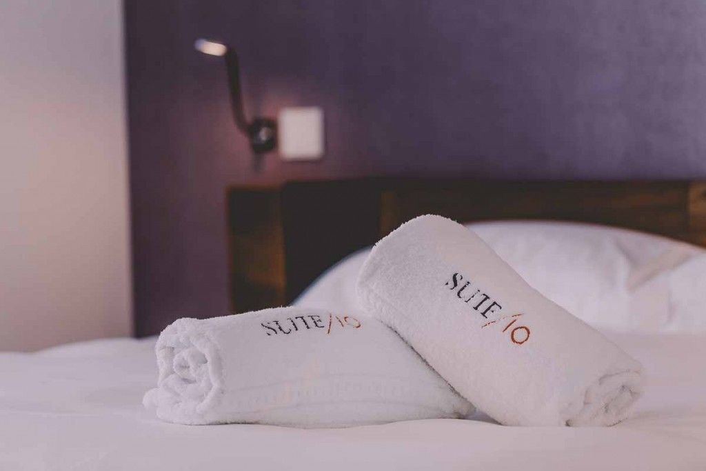 A neatly made bed with two white towels labeled "SUITE 10" on a white bedspread.