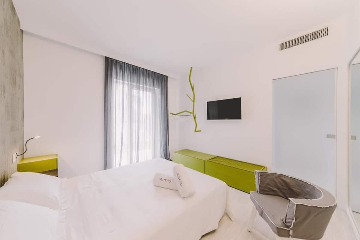Una habitación de hotel con una cama, una mesita de noche verde, un televisor montado en la pared y una silla.