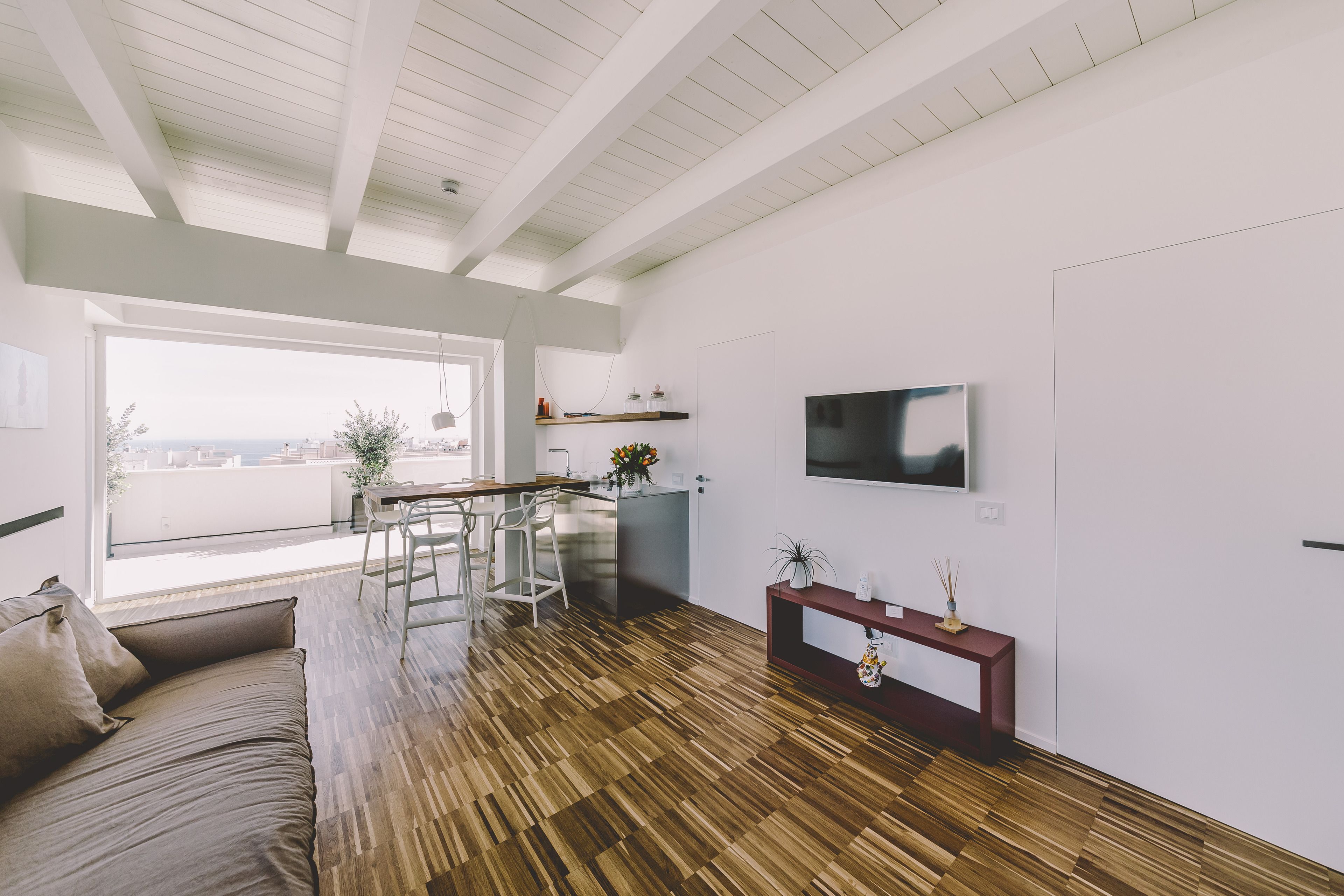 A modern living room with a wooden floor, a sofa, a TV, and a balcony with a view.