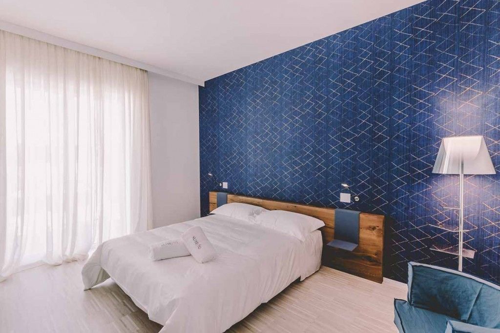 Habitació d'hotel amb un llit, una tauleta de nit, una làmpada i una paret amb un disseny blau.