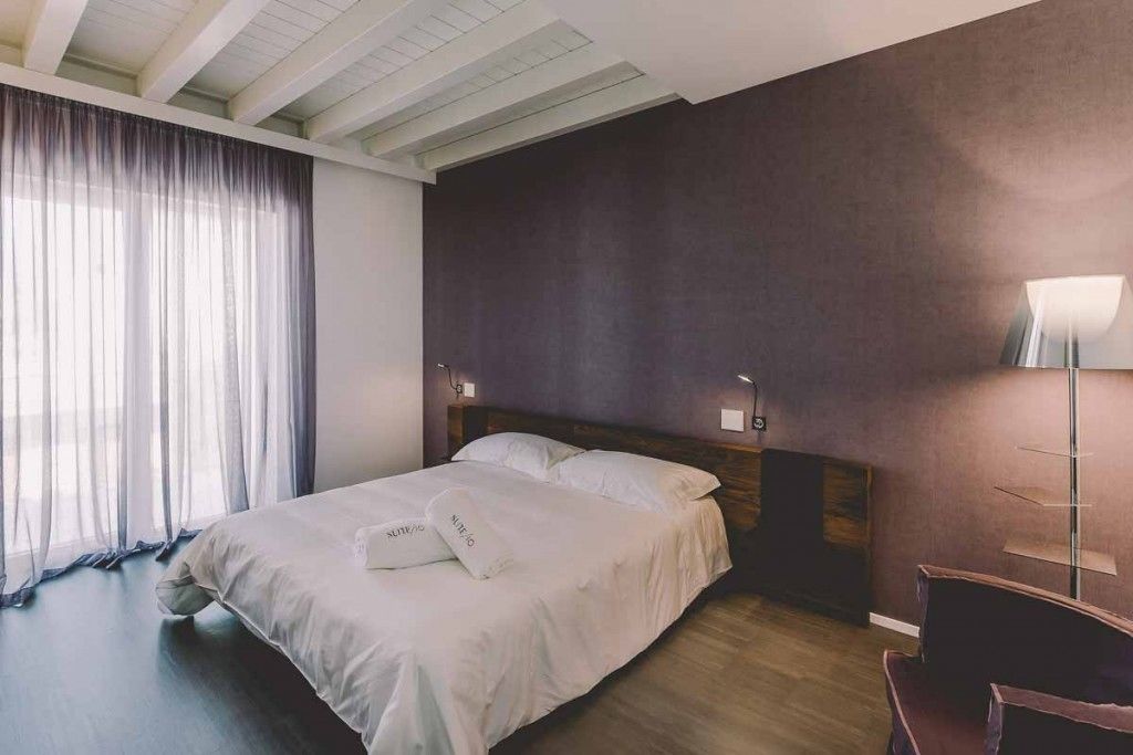 A modern bedroom with a large bed, wooden headboard, and a bedside table with a lamp.