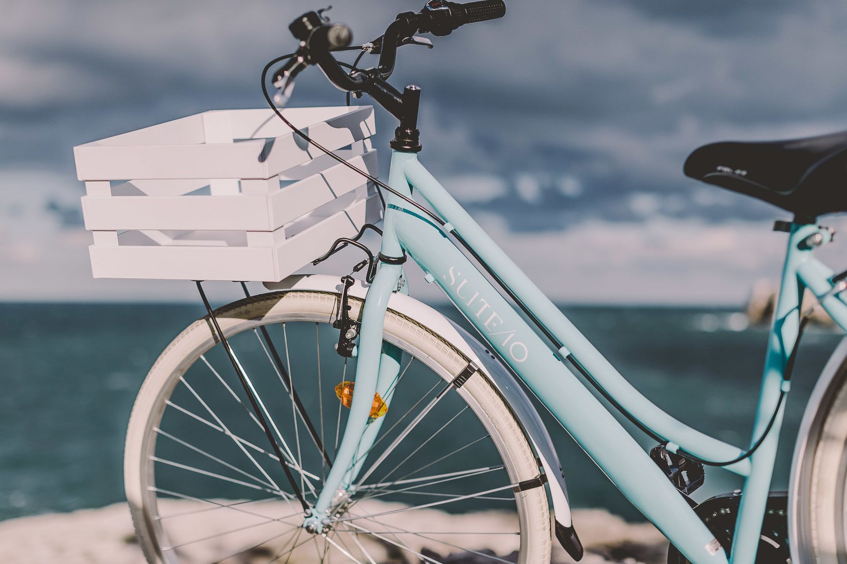 A light blue bicycle with a white basket and black seat, parked by the seaside.