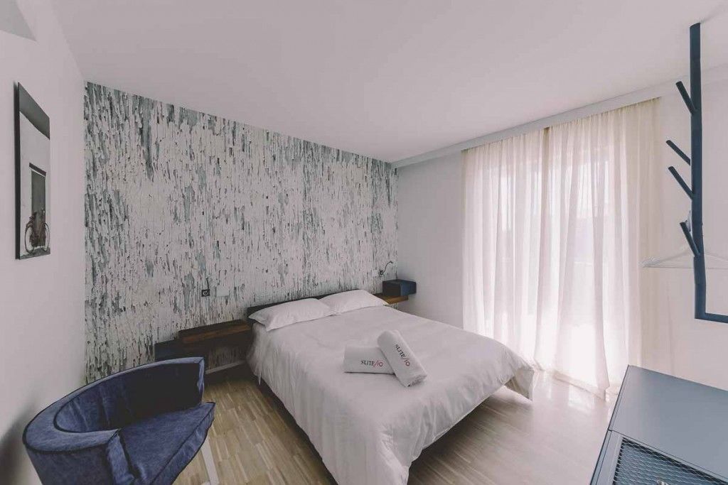 Une chambre d’hôtel moderne équipée d’un lit, d’une chaise, d’un bureau et d’une grande fenêtre avec des rideaux.