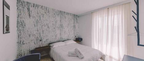 Une chambre d’hôtel moderne équipée d’un lit, d’une chaise, d’un bureau et d’une grande fenêtre avec des rideaux.