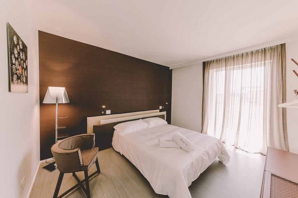 A hotel room with a bed, a chair, a lamp, and a large window with curtains.