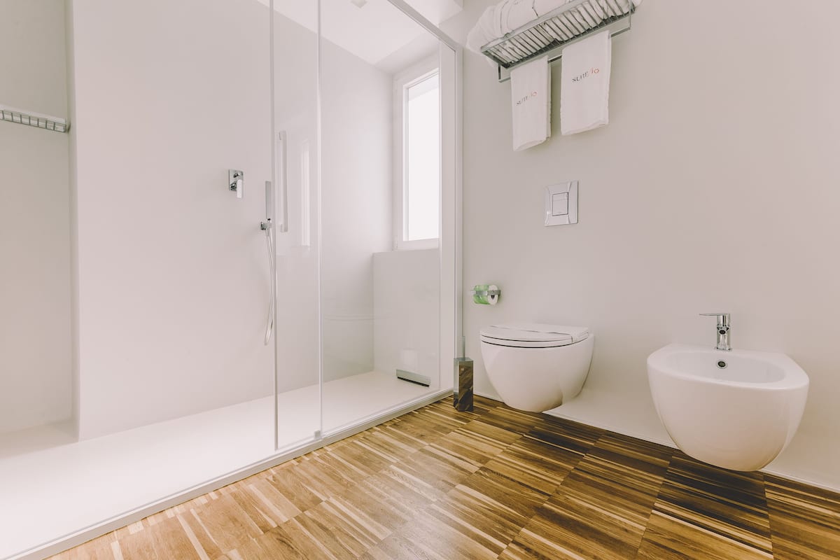 Un baño moderno con cabina de ducha de vidrio, un lavabo blanco y suelo de madera.