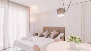A modern hotel room with a large bed, a bedside table, a round dining table, and a vase of flowers. - Suite 10 - Home, Design & Spa (Polignano a Mare)