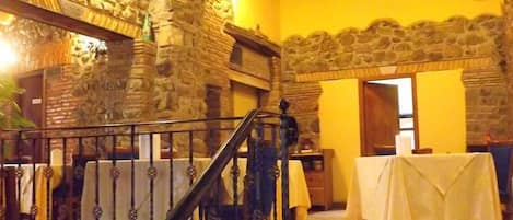 Un restaurante con paredes de piedra, una escalera y mesas dispuestas para comer.