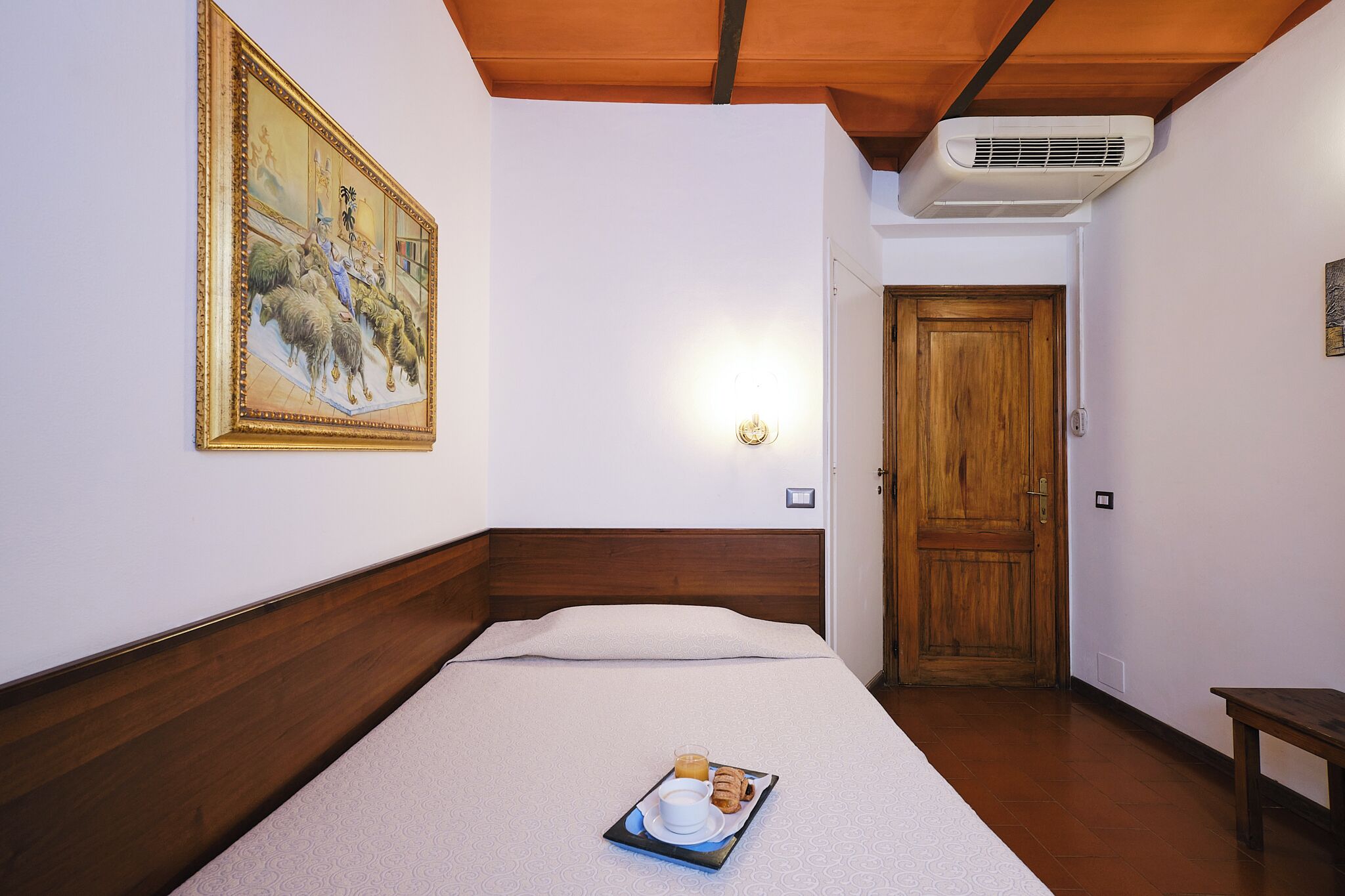 Una camera d'albergo con un letto, un vassoio con la colazione, una porta in legno e un quadro appeso al muro.