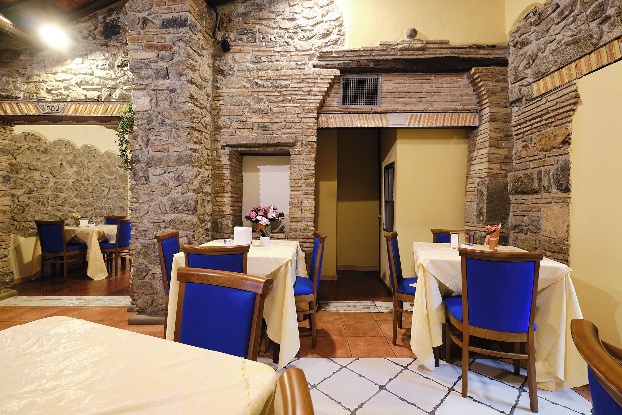 A restaurant with stone walls, blue chairs, and tables set with white tablecloths.