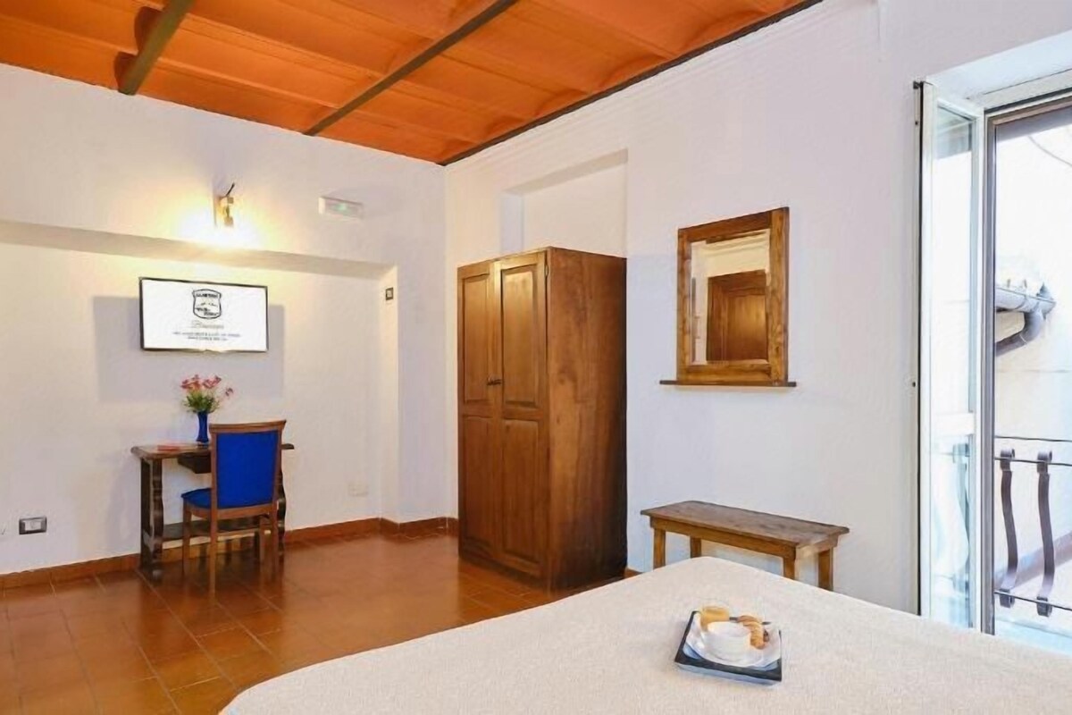 Una habitación con techo de madera, un escritorio con una silla, un armario de madera y una puerta que da a un balcón.