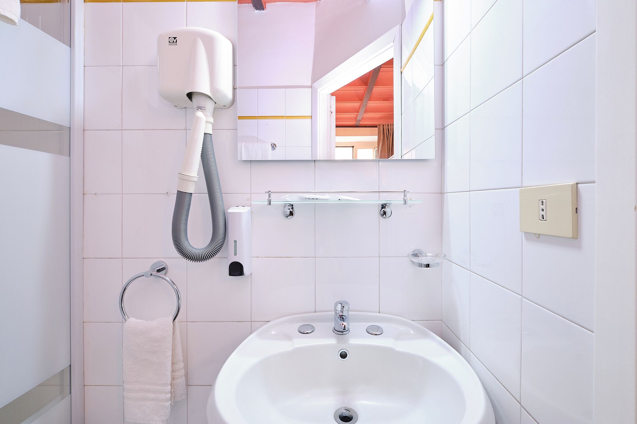 Un baño con un lavamanos blanco, un tozaleto, un espejo y un secador de pelo fijado a la pared.