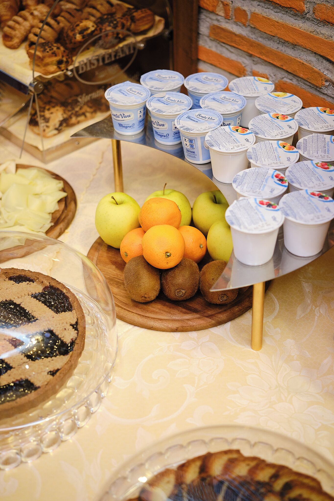 A display of food items including apples, oranges, kiwis, and pastries.