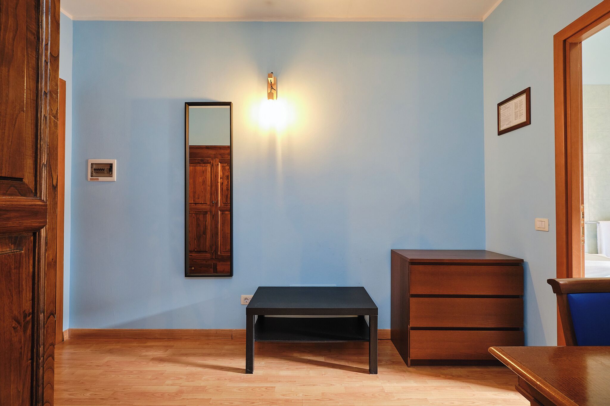 A room with a wooden floor, a black table, a wooden cabinet, and a wall-mounted light fixture.
