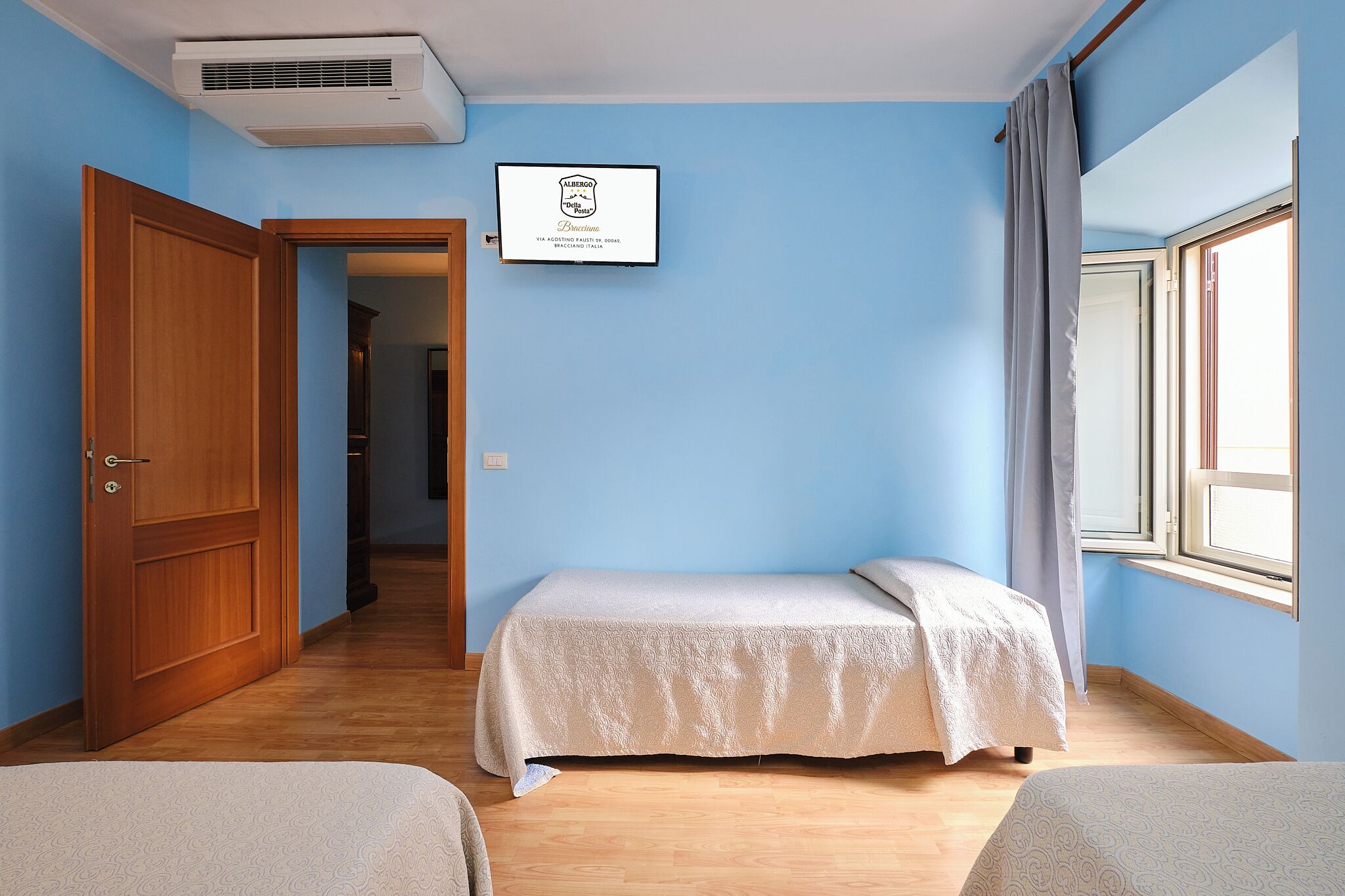Una stanza con un letto, una finestra, una porta e un certificato incorniciato al muro.