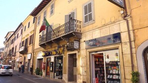 A street view with a yellow building featuring a balcony with a flag, a bookstore, and a restaurant. - Albergo della Posta (Bracciano)