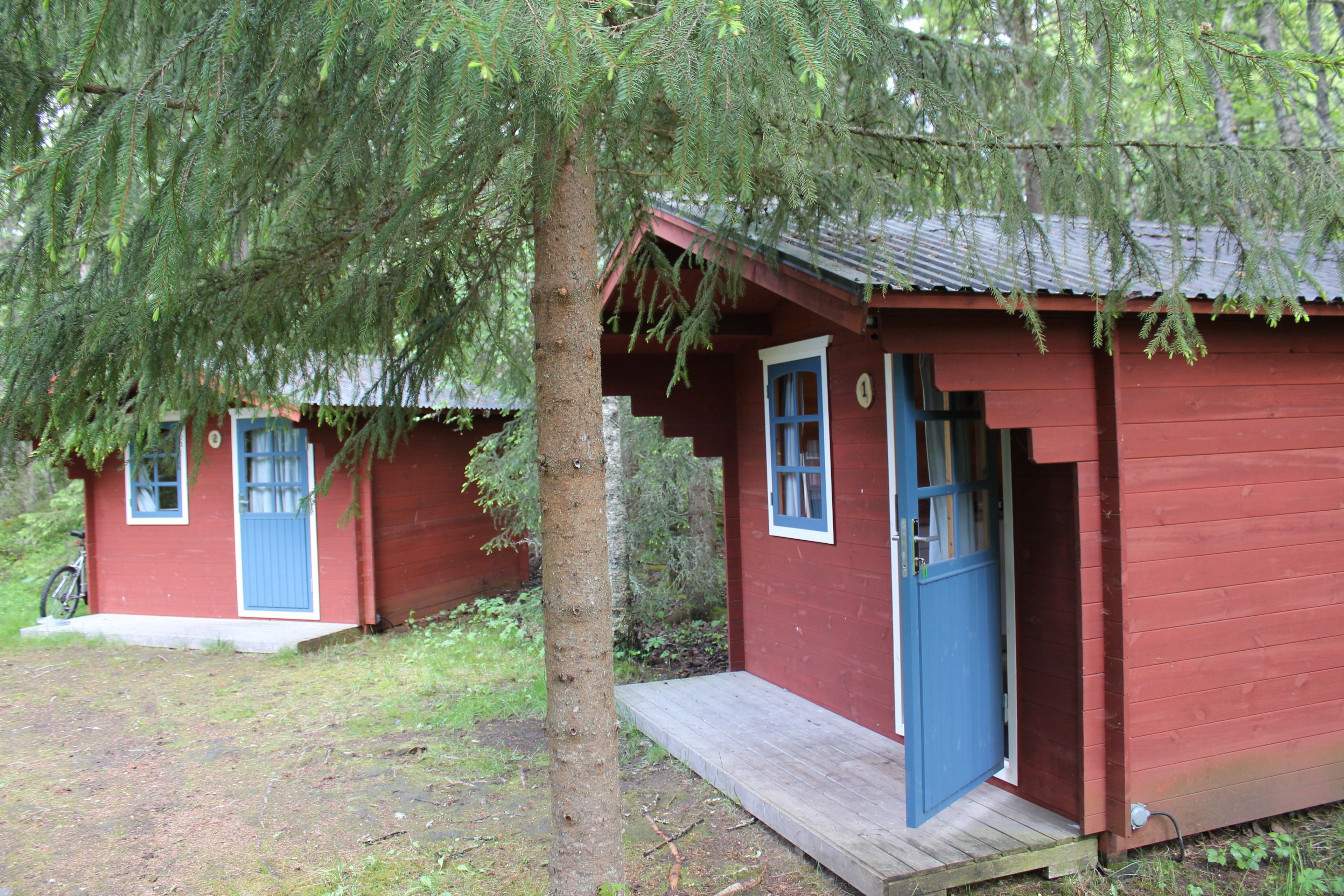 Two red cabins with blue doors and windows, surrounded by trees.