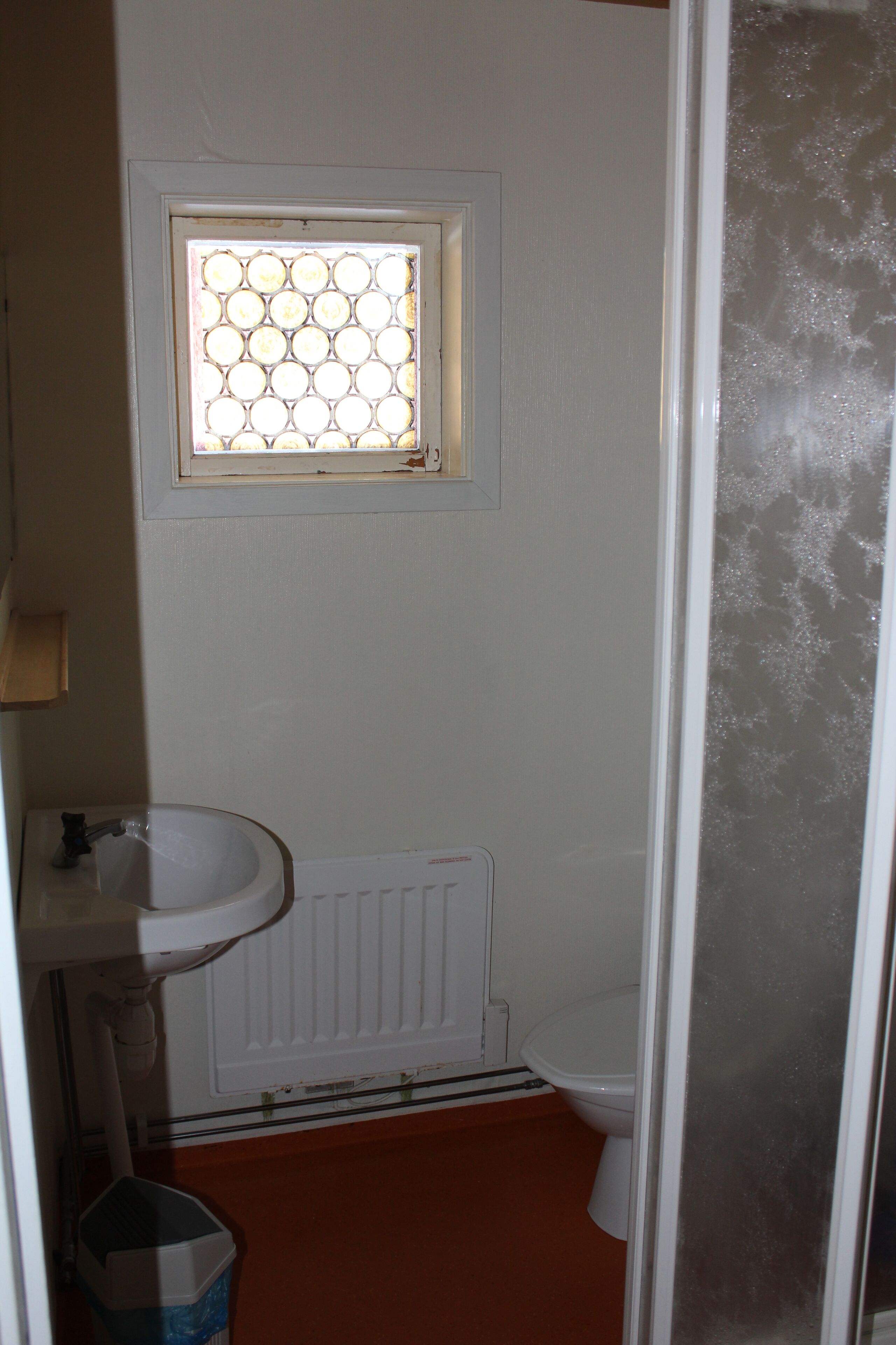 A bathroom with a white sink, a toilet, and a window with a patterned glass door.