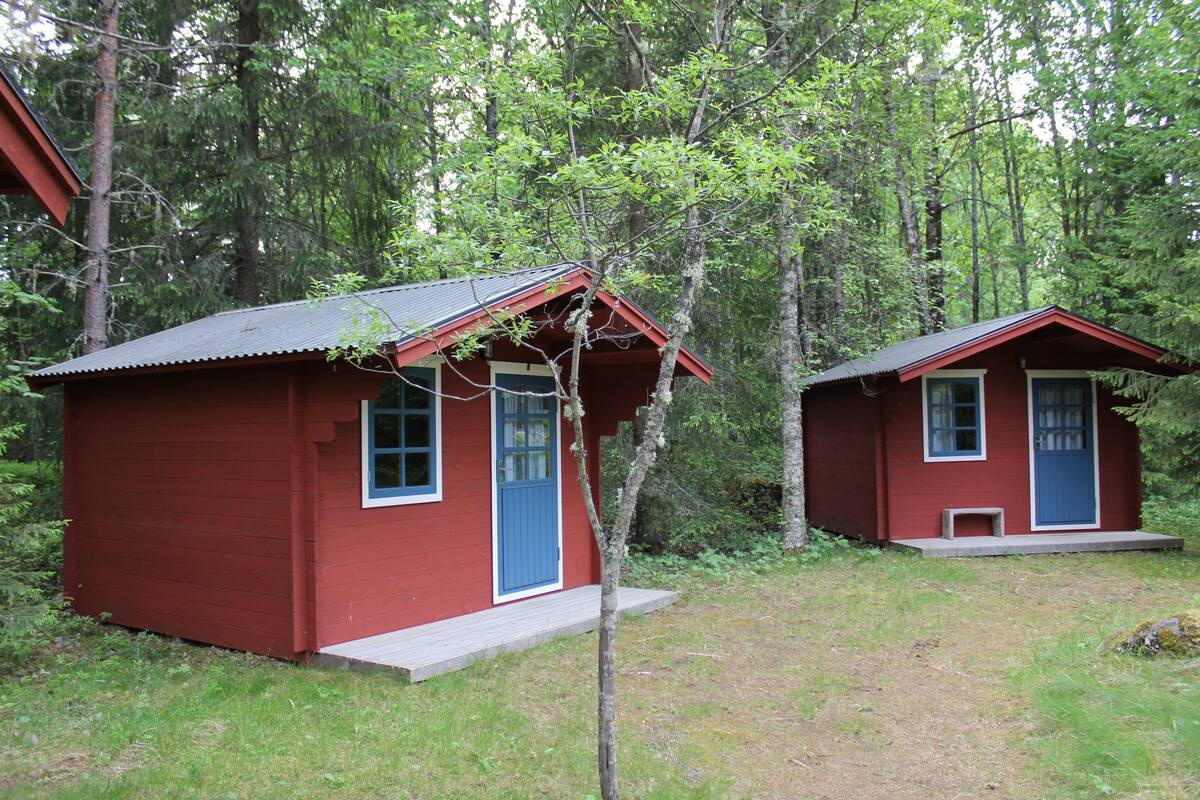Two small red cabins with blue doors and windows, surrounded by dense forest.