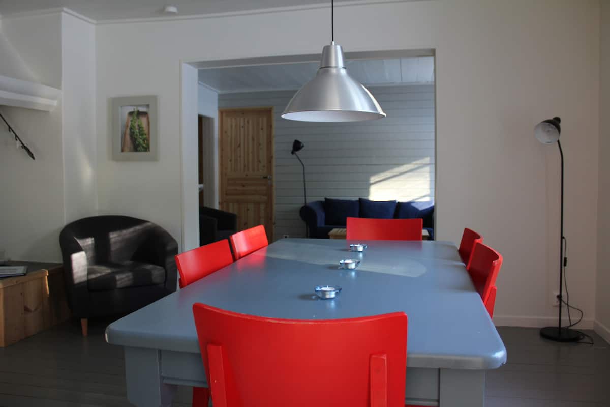 A dining area with a blue table and red chairs, a pendant light, and a framed picture on the wall.